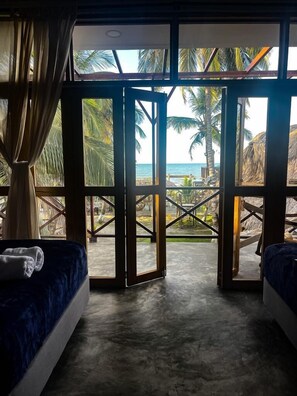 A room with a view of the beach, featuring two beds, a large glass door, and a concrete floor. - CASA ORIGEN BOUTIQUE (San Bernardo del Viento)