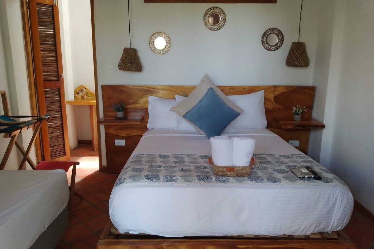 A neatly arranged bedroom with a wooden headboard, a bed with white bedding and a blue pillow, a bedside table with a lamp, and a small potted plant.