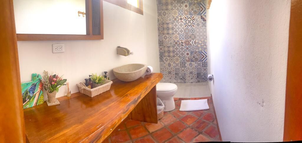 Une salle de bain avec un meuble-lavabo en bois, un grand lavabo sur pied, des toilettes blanches et un mur de douche orné d’un motif.