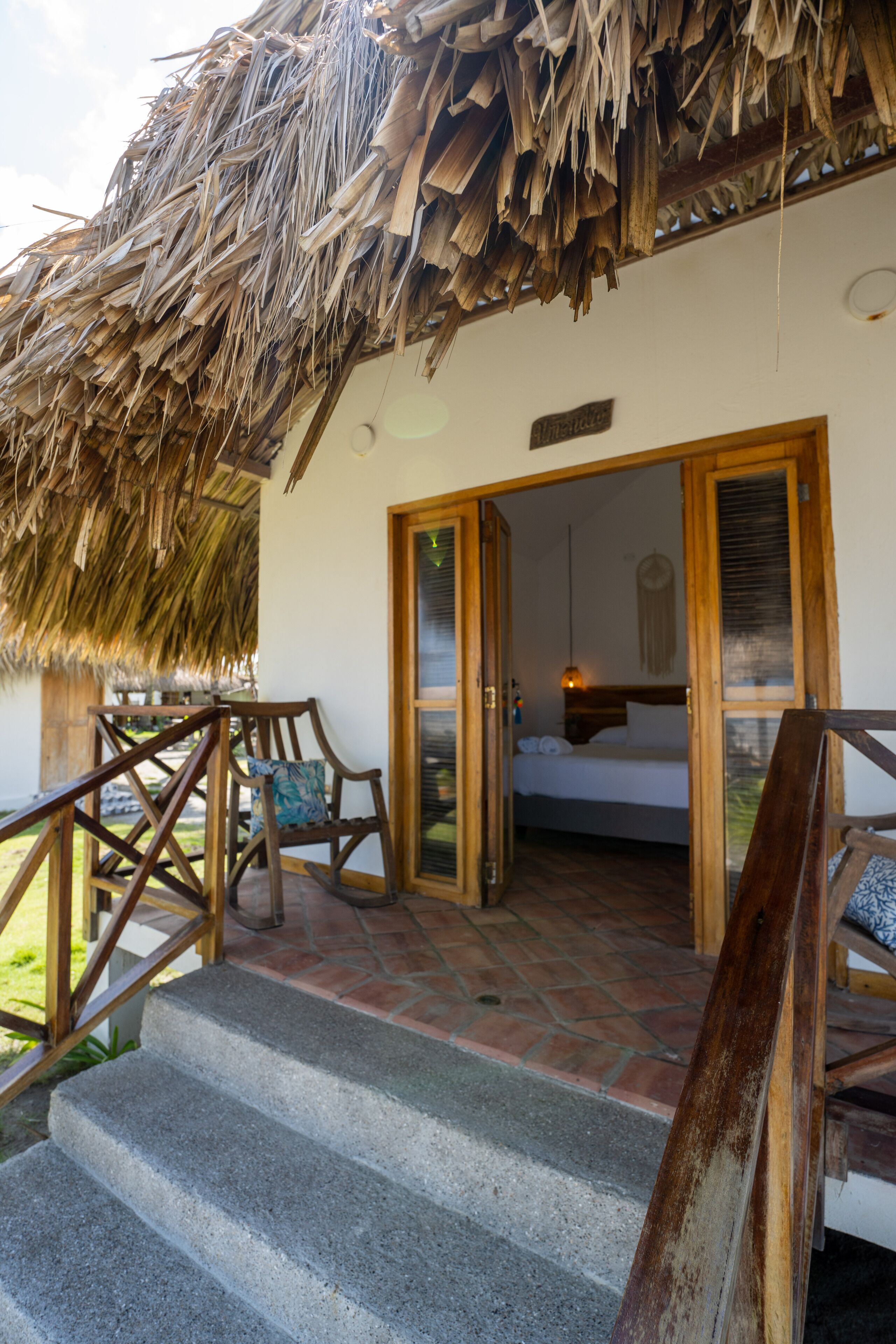 A room with a bed, a wooden chair, and a thatched roof.