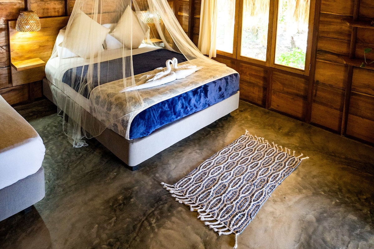 A room with a bed, a ceiling fan, a mosquito net, and a window with curtains.