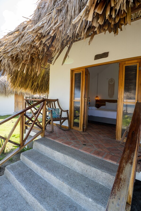 A thatched-roof structure with a bed, a chair, and a staircase leading to a room. - CASA ORIGEN BOUTIQUE (San Bernardo del Viento)