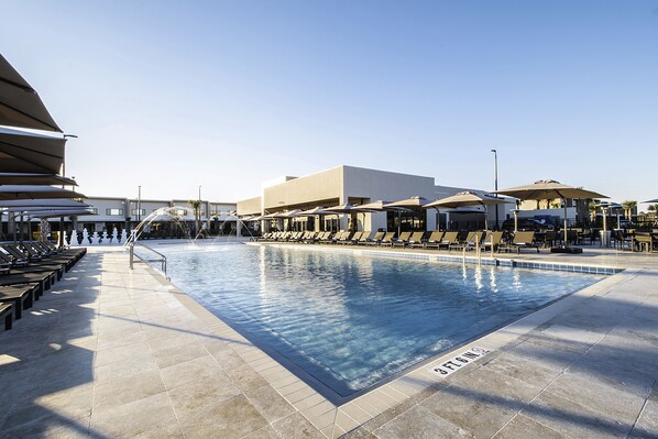 A swimming pool with sun loungers and umbrellas, surrounded by a building with a flat roof.