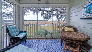 A covered porch with wicker furniture, a blue patterned rug, and a view of a field and trees.