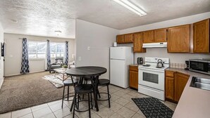Une cuisine compacte avec des meubles en bois, un réfrigérateur blanc, une cuisinière et un four à micro-ondes. On y trouve également un coin repas avec une table et des chaises.