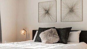 Un lit bien fait, avec un oreiller moelleux, une lampe de chevet et deux œuvres d’art abstraites accrochées au mur.