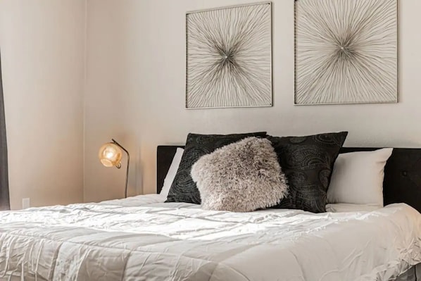 A neatly made bed with a fluffy pillow, a bedside lamp, and two abstract wall art pieces.