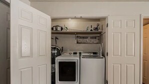 Une buanderie équipée de deux machines à laver et deux sèche-linge superposés, d’une étagère contenant des produits de lessive et d’un panneau placé au-dessus de l’étagère.