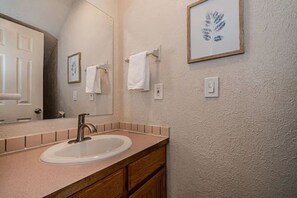 Un baño con lavamanos, espejo y una obra de arte enmarcada en la pared.
