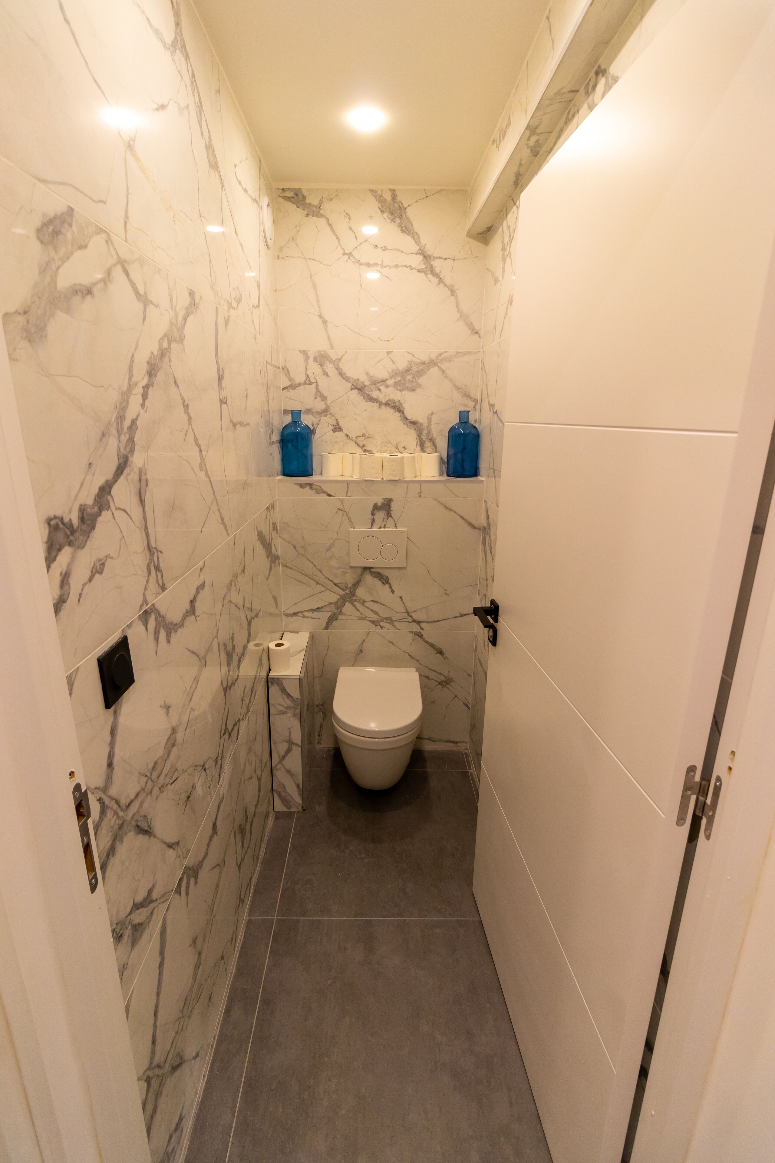 Een kleine badkamer met marmeren wanden, toilet en wastafel.