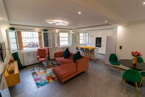 Una sala moderna con un sofá modular, una mesa de comedor con sillas y una zona de cocina.