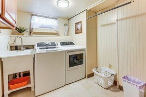 A laundry room with a washing machine, dryer, sink, and a small window with a curtain.