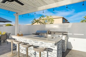 An outdoor kitchen with a stone island, bar stools, and a grill. - Luxurious desert home w/ pool & jacuzzi! (Coachella)