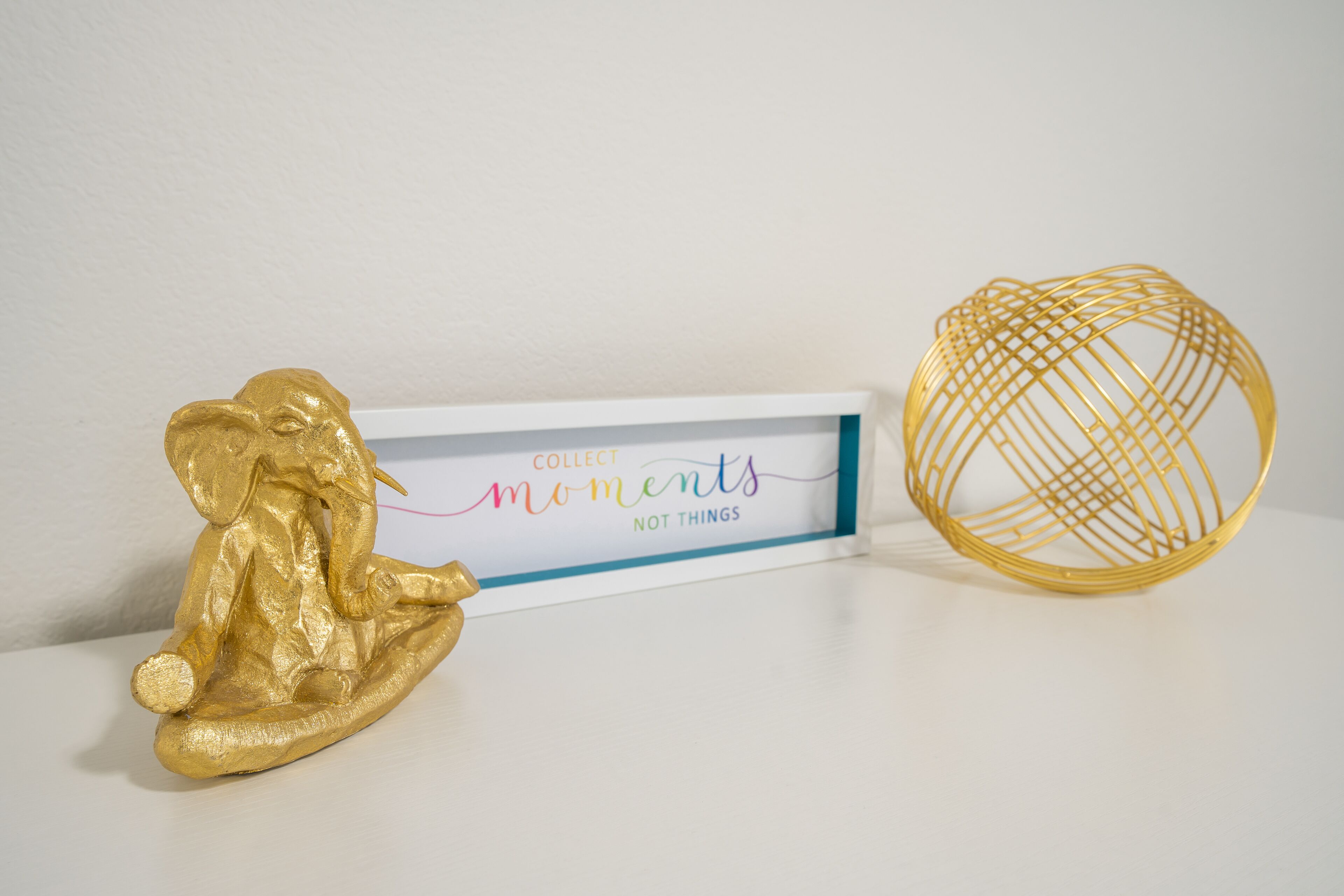 Eine goldfarbene Figur einer Person, ein gerahmtes Schild mit Text und ein goldfarbenes Drahtmodell.