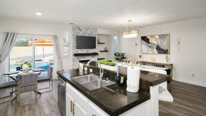 Une cuisine moderne dotée d’un îlot central, d’un coin repas avec une table en verre et d’une vue sur une piscine.