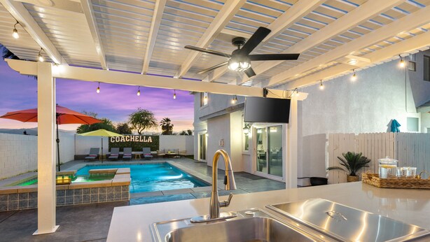 Un espace cuisine extérieur moderne, doté d’une piscine, d’un ventilateur de plafond et d’une enseigne sur laquelle on peut lire « COACHELLA ».