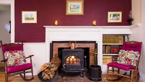 Une pièce à l’ancienne, dotée d’une cheminée, de deux fauteuils à bascule avec des coussins à motifs floraux et d’une bibliothèque remplie de livres.