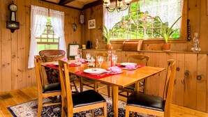 Une salle à manger en bois avec une table dressée pour quatre personnes, entourée de chaises dotées de coussins noirs.