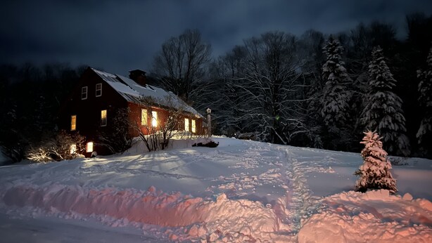 Un paysage enneigé avec une maison illuminée par des lumières chaleureuses.