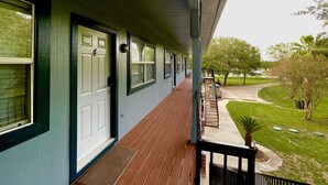 A covered porch with a wooden deck, a white door, and a window with a black frame. - Lovely 1 bedroom apartment Pearland - Wi-Fi - Roku TV (Pearland)