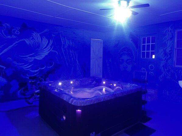 Una habitación con bañera de hidromasaje, ventilador de techo y un mural en la pared.