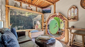 Un intérieur rustique agrémenté d’une grande fenêtre, d’une porte verte ronde et d’un coin salon confortable.