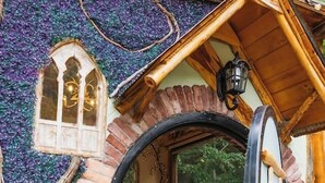 Une cabane rustique dotée d’une fenêtre circulaire, d’une porte en bois et d’une petite fenêtre surmontée d’un arc décoratif.