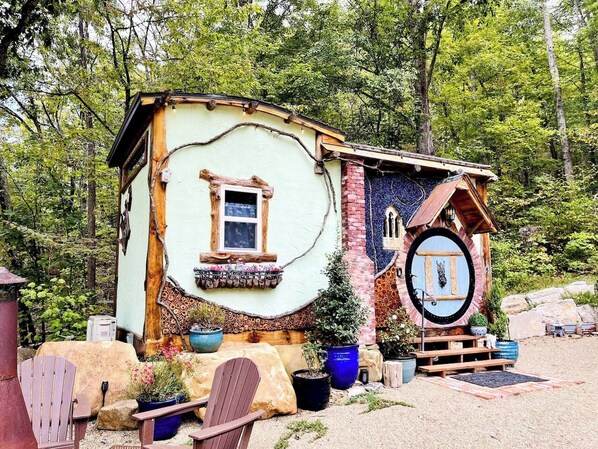 A rustic cabin with a circular door, a small window, and a wooden porch.