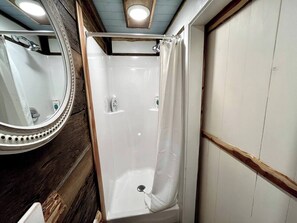 A small, enclosed shower area with a shower curtain, a mirror, and a wooden floor.