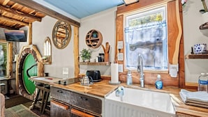 Une cuisine rustique avec des poutres en bois, une porte verte, un évier et une fenêtre donnant sur un paysage agréable.