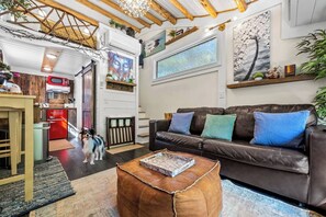 A living room with a brown leather sofa, a coffee table, a dog, and a kitchen area with a red refrigerator. - Serenity Tiny House Located Near Top Attractions! (Sevierville)