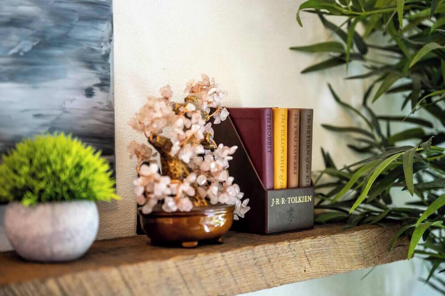A wooden shelf with a small potted plant, a decorative vase with flowers, and a stack of books.