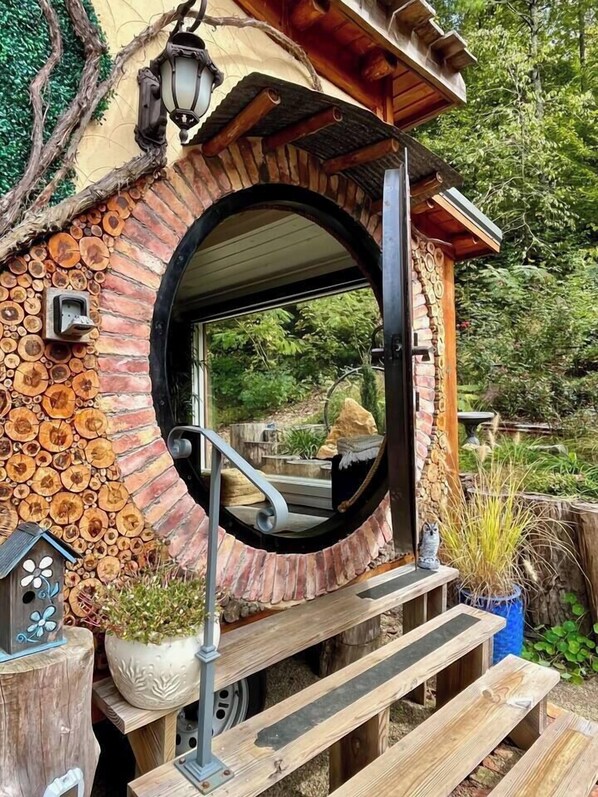 A circular structure with a wooden exterior, a metal door, and a small porch area with steps leading up to it. - Serenity Tiny House Located Near Top Attractions! (Sevierville)