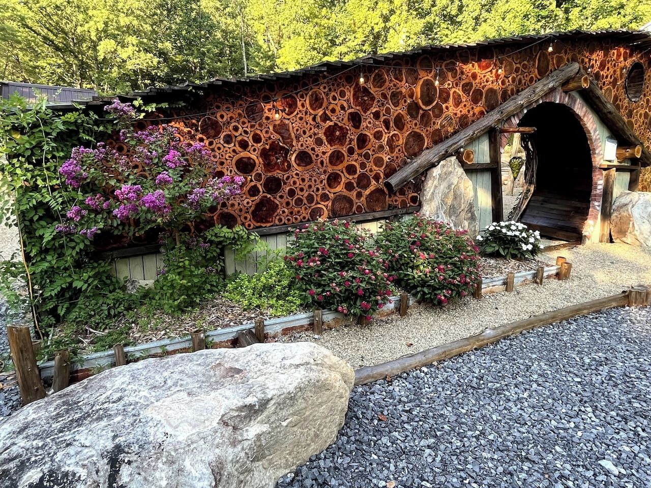 Un pont de pedra rústic amb entrada de túnel, envoltat de grava i plantes en flor.