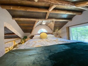 Cozy bedroom with a sloped ceiling and exposed beams, featuring a large bed and a small window.
