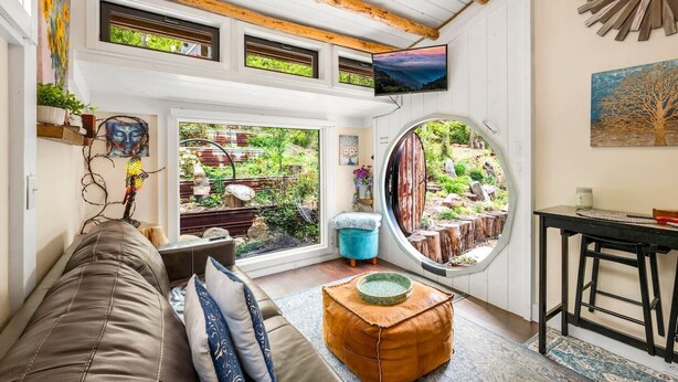 Um quarto aconchegante com um sofá, uma mesa redonda, uma televisão e uma janela grande com vista para um jardim.