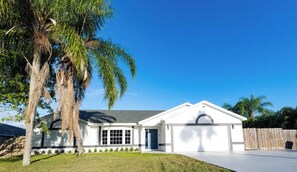 Stunning single-story home with a central entrance and two windows on each side, set amidst a beautifully manicured lawn and a wooden fence.