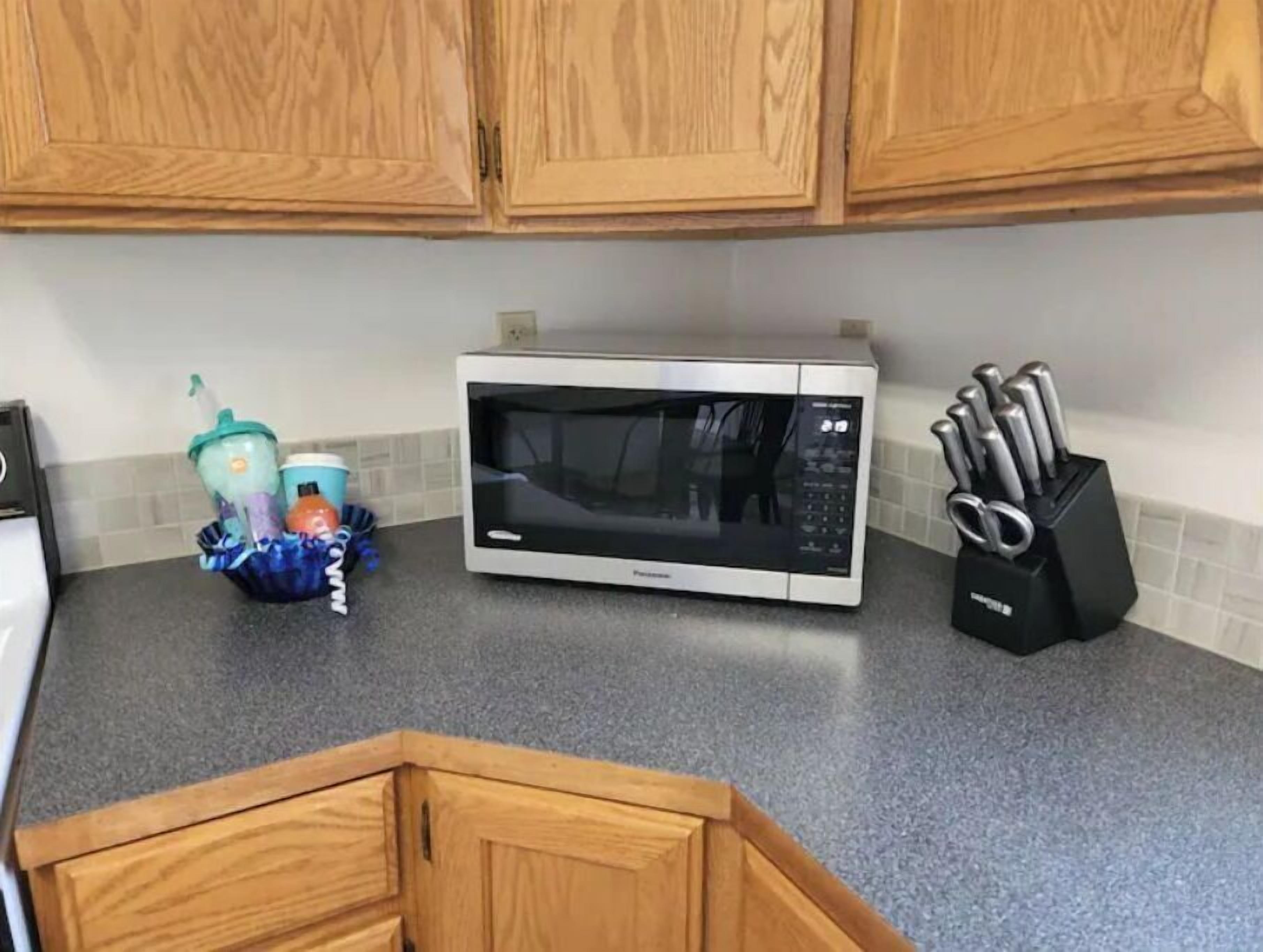 A kitchen with wooden cabinets, a microwave, and a knife block on the countertop.