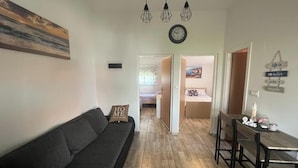 A living room with a sofa, a dining table with chairs, a clock, and a painting on the wall. - Vacation apartment, quiet part. Perfect for your vacation! (Vir)