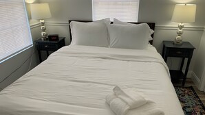 A neatly made bed with white linens, two bedside tables with lamps, and a clock on one table. - Spacious 4-bedroom house  walking distance to Mercedes Benz Stadium & Downtown (Atlanta)