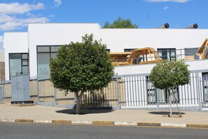 A modern building with large windows, a fenced area, and two trees in front. - TaTe Village - Hostel (Windhoek)