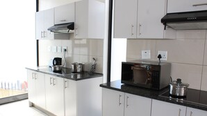 A modern kitchen with white cabinets, a microwave, and a stove. - TaTe Village - Hostel (Windhoek)