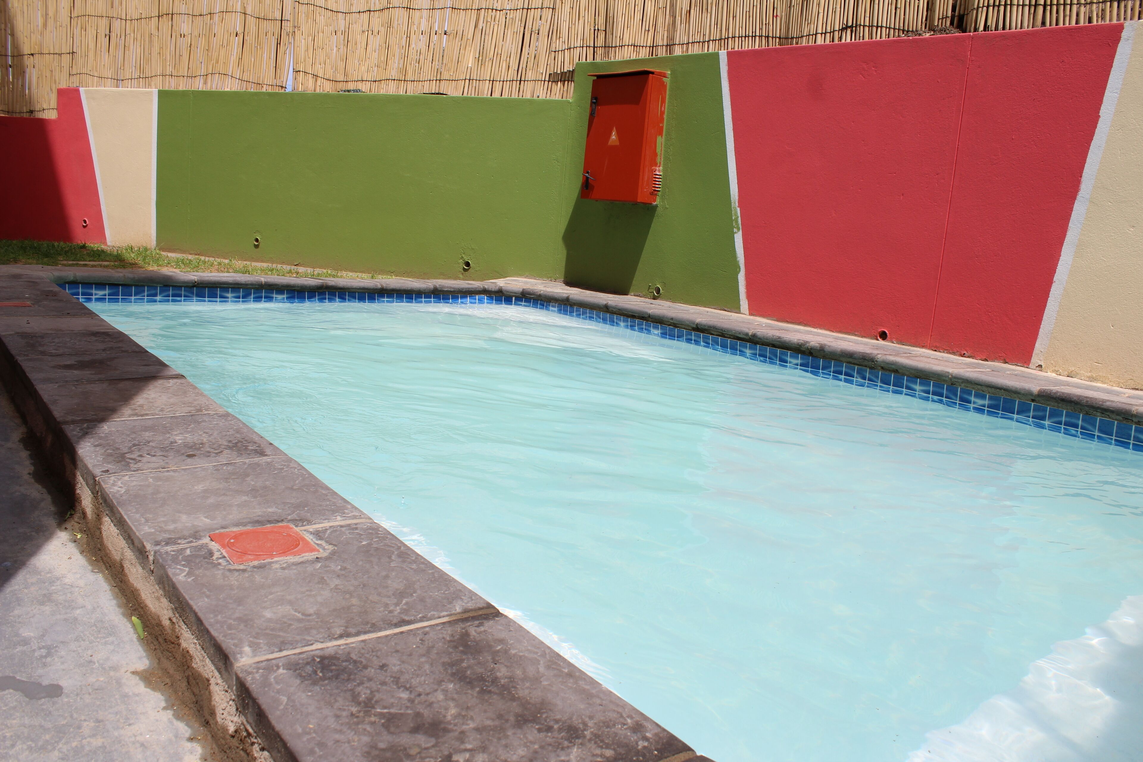A swimming pool with a tiled edge, surrounded by a wall with a red and green color scheme.