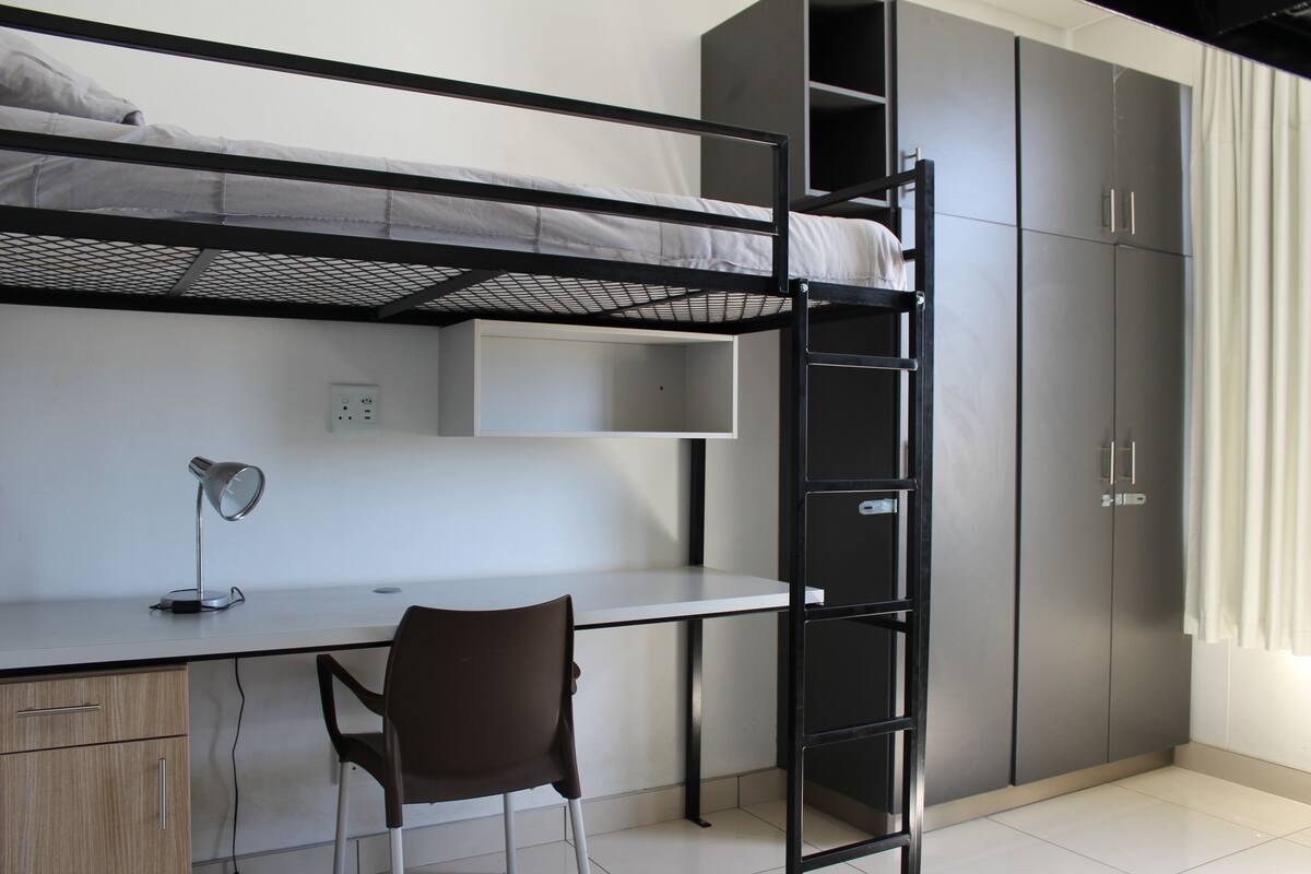 A bunk bed, desk, chair, and wardrobe in a room.