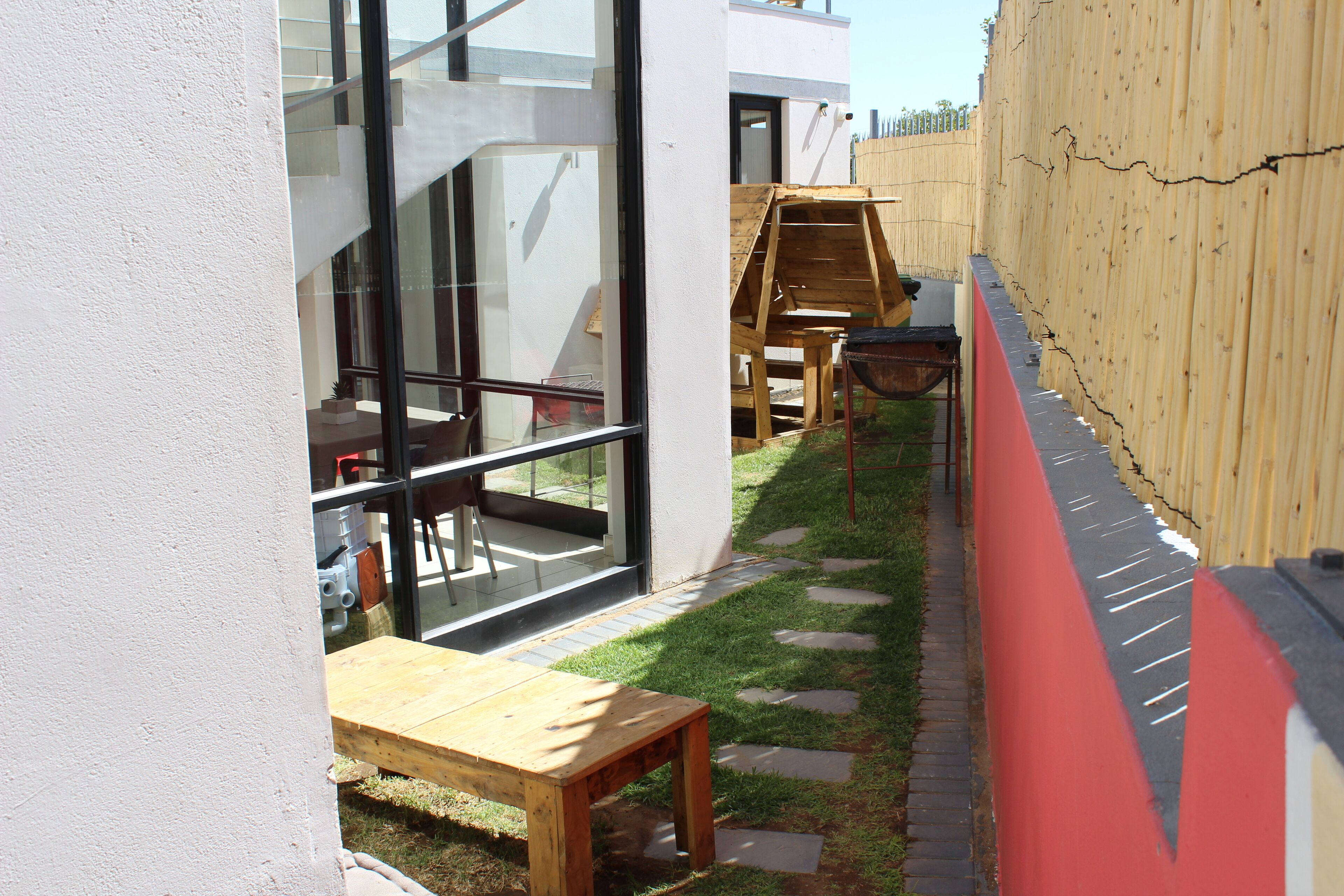 Un patio con mesa y sillas de madera, una pequeña estructura de juego de madera y un muro rojo y negro.