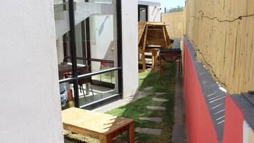 Un patio con mesa y sillas de madera, una pequeña estructura de juego de madera y un muro rojo y negro.