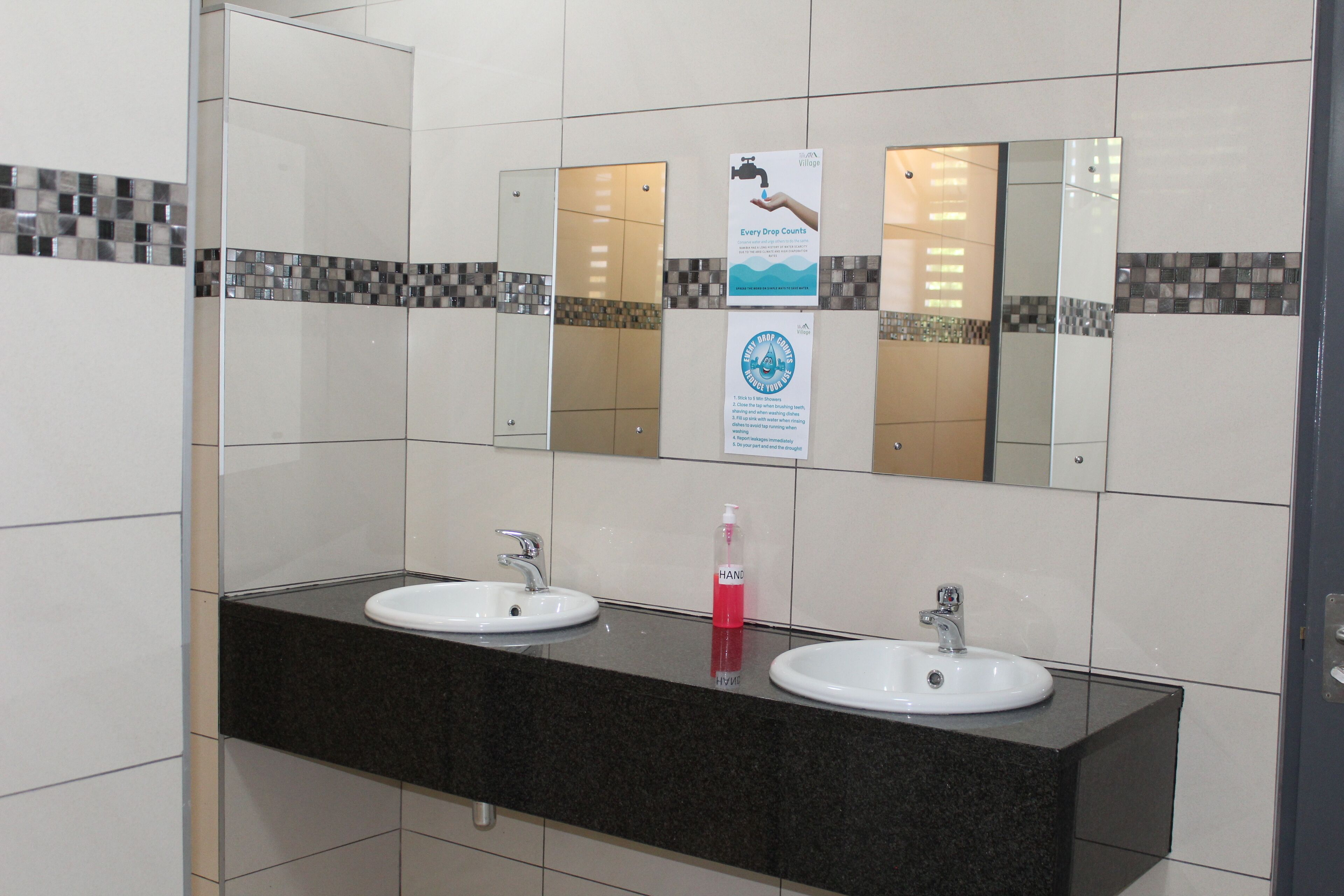 A bathroom with two sinks, a mirror, and a hand sanitizer dispenser.
