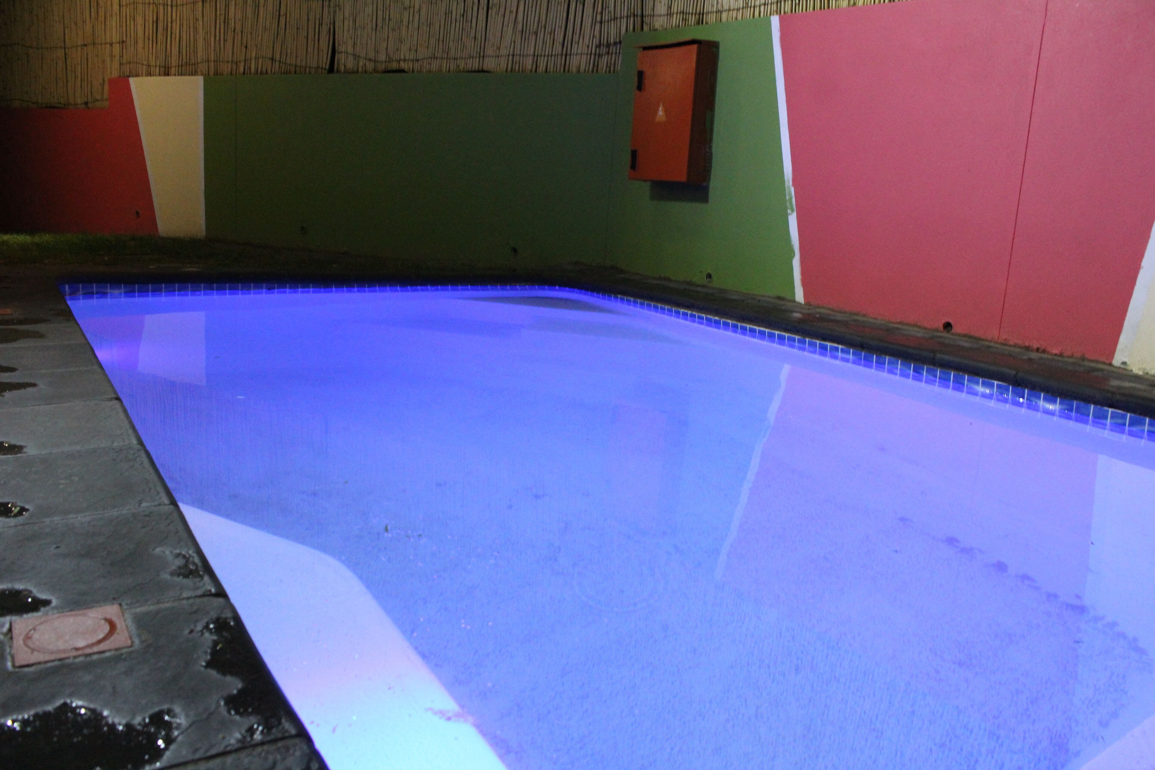 Piscina interna com piso iluminado em azul, rodeada por paredes verdes e vermelhas.