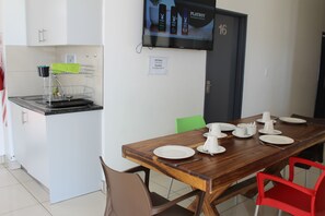 A dining area with a wooden table set for four, a kitchen area with a sink and dish rack, and a door marked with the number 16. - TaTe Village - Hostel (Windhoek)