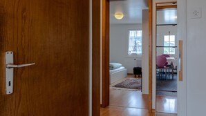 A wooden door leading to a room with a bed, a window, and a dining area with chairs.